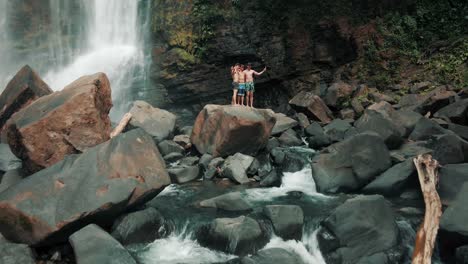 Turistas-Parados-Sobre-Una-Enorme-Roca-Y-Tomando-Fotos-En-Las-Cascadas-De-Nauyaca-En-La-Provincia-De-Puntarenas,-Costa-Rica---Disparo-De-Drones