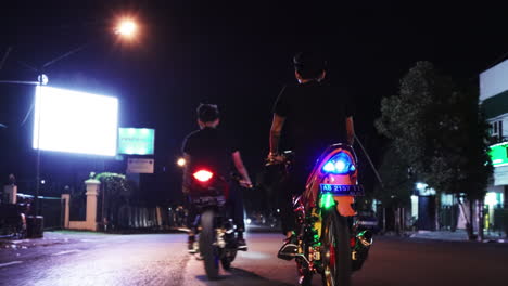 Toma-De-Seguimiento-Siguiendo-De-Cerca-A-Dos-Hombres-En-Motocicletas-Conduciendo-Por-Las-Calles-De-La-Ciudad-De-Yogyakarta,-Indonesia,-Por-La-Noche.