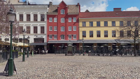 Lilla-Torg-in-Malmo-features-an-old-phone-booth,-classic-light-poles,-cobble-stones,-and-colourful-houses,-with-people-walking-in-the-background