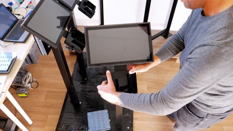 bird's-eye-view-in-a-brightly-lit-room-of-a-male-technician-mounting-a-black-plastic-support-below-a-free-standing-shelf