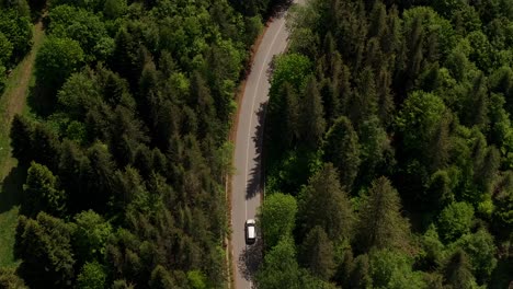 Car-driving-on-a-winding-tarmac-road-through-green-forests-in-the-mountains,-tracking-aerial-shot