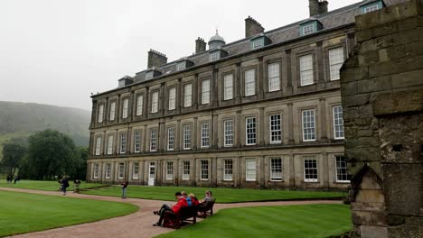 The-gardens-of-the-Holyrood-Palace,-royal-residence-in-Edinburgh,-Scotland-with-people-walking-and-sitting-on-a-bench