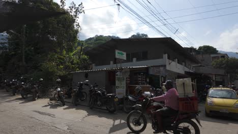 Street-scene-in-Minca,-Colombia-with-motorcycles-parked-along-the-road-and-people-walking-under-shaded-areas