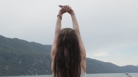 Blonde-young-woman-lifts-her-arms-yoga-pose-in-natural-lake-bird-fly-near-by-sea