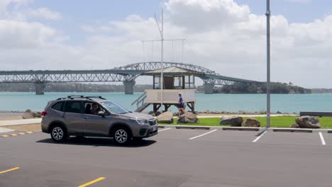 Man-running-another-man-driving-SUV-car-and-parking-near-lifeguard-house,-Auckland,-New-Zealand