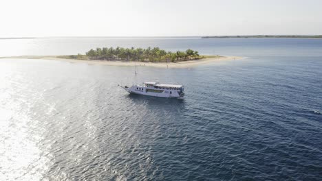 Tourist-boat-anchored-next-to-Pulau-Bedil,-a-tiny-Indonesian-beautiful-island-off-the-coat-of-Lombok,-Aerial-view