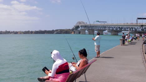 People-fishing-at-westhaven-on-sunny-day,-Harbour-bridge-in-background,-Auckland,-New-Zealand