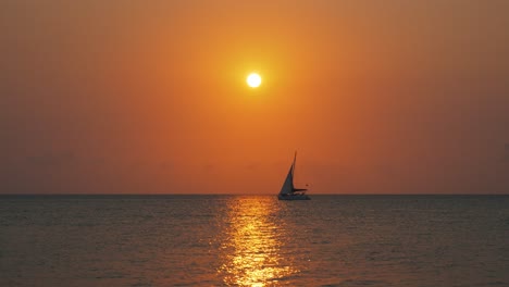 Small-saling-boat-alone-on-calm-ocean-horizon-during-beautiful-sunset