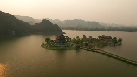 Aerial-circling-wide-angle-plan-of-Ninh-Binh-temple-with-sun-reflection-in-lake,-Vietnam