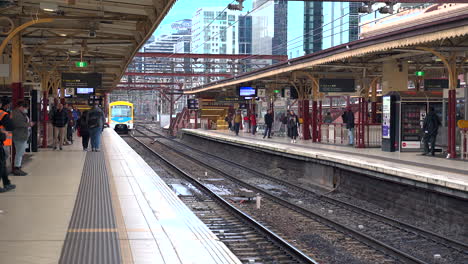 Metro-train-arrives-at-Melbourne-station-platform,-commuters-wear-face-mask