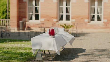 Outdoor-garden-table-setup-with-a-red-juice-dispenser-and-bottles,-ready-for-a-gathering