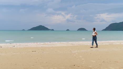 A-woman-walks-along-the-serene-beach-of-Con-Dao-island,-Vietnam-on-a-cloudy-day