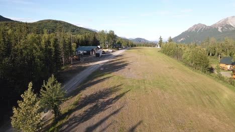 Drohnenaufnahmen-Eines-Langsamen-Fluges-über-Eine-Private-Graspiste-Mit-Häusern-Und-Gebäuden-An-Den-Seiten-In-Den-Talkeetna-Mountains