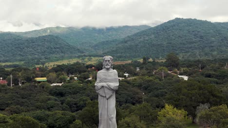 A-drone-flying-near-the-Cristo-Penitente-in-La-Caldera,-Salta,-Argentina,-capturing-its-imposing-presence-against-the-scenic-backdrop