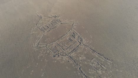 Aerial,-reverse,-drone-shot,-around-a-water-tower-drawing-in-sand,-at-a-beach,-on-a-sunny-evening,-in-Langeoog,-Germany