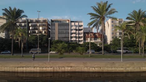 Seitliche-Luftaufnahmen-Entlang-Des-City-Lake-Boulevard-Von-Rio-De-Janeiro-Mit-Menschen,-Die-Ihre-Morgengymnastik-Beim-Joggen-Und-Fahrradfahren-Machen