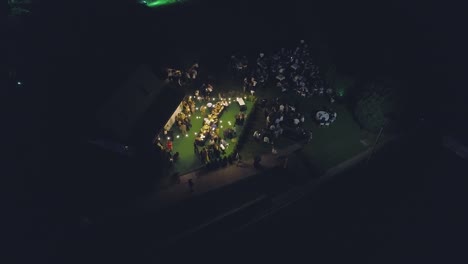 Toma-Aérea-Descendente-A-Una-Celebración-De-Boda-Durante-La-Noche-En-Un-Jardín-Verde.