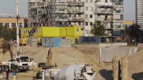 Building-foundation-hole-in-Vienna,-Austria,-with-construction-workers-and-machinery-inside-and-an-apartment-building-in-the-background