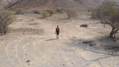 Aerial-tracking-shot-from-drone-of-an-young-male-walking-in-a-rocky-desert-valleys-in-Hatta,-United-Arab-Emirates