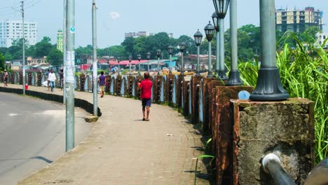 young-street-boy-in-red-shirt-flying-kite-near-light-poles-in-outskirts-of-Sylhet,-Bangladesh