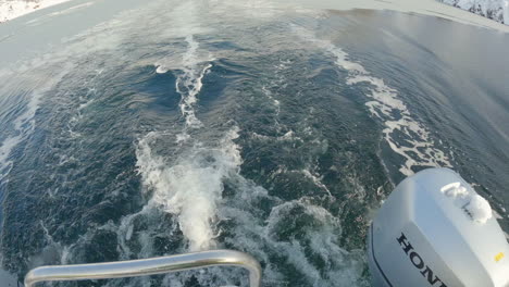 Tilting-up-shot-from-an-outboard-motor-on-a-boar-to-an-ice-covered-bay-with-beautiful-mountains-in-the-background