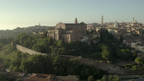 Drone-slow-push-in-towards-medieval-church,-rises-to-reveal-medieval-city-behind,-showing-Renaissance-architecture-finally-turns-to-right-dramatically-showing-more-buildings-and-churches