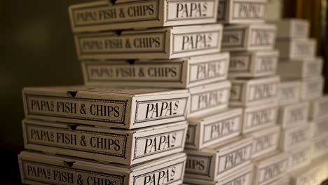 PAPAs-fish-and-chips-box-pile,-placing-another-box-down-in-slow-motion