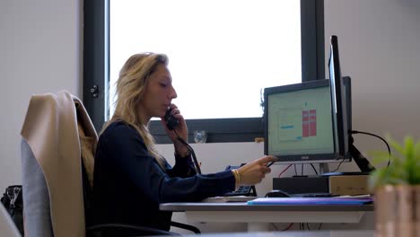 Slow-motion-shot-of-a-woman-answering-an-incoming-phonecall-at-her-desk