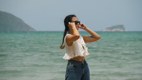 Frau-Steht-An-Einem-Sonnigen-Strand-In-Con-Dao,-Vietnam,-Trägt-Eine-Sonnenbrille-Und-Ein-Weißes-Oberteil