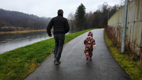 Grandfather-and-granddaughter-is-running-by-the-river-during-the-rain-in-autumn