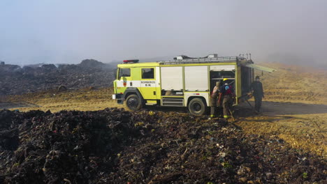 Aéreo,-Drone-De-Bomberos-Sacando-Una-Manguera-De-Un-Camión-De-Bomberos-En-Un-Incendio-Forestal,-Rodeado-De-Humo,-Día-Soleado,-En-Santo-Domingo,-República-Dominicana