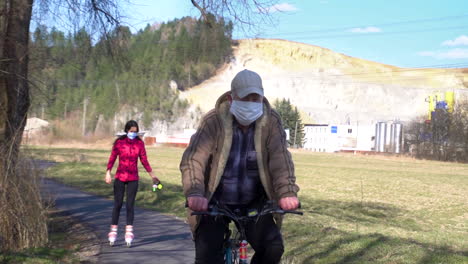 Un-Hombre-Montando-Una-Bicicleta-Con-Una-Niña-En-Patines-Sosteniendo-Una-Correa-De-Su-Perro-Y-Ambos-Usando-Una-Máscara-Cerca-De-Bratislava,-Eslovaquia-Durante-El-Brote-De-Coronavirus.