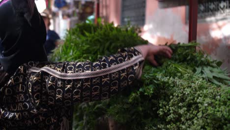 Woman-buying-herbs-and-vegetables-from-the-local-market,-fresh-produce-and-busy-crowded-streets