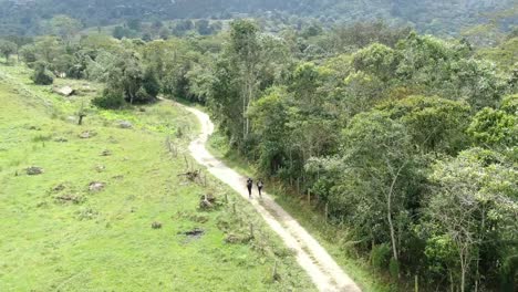 Two-hikers-walking-on-a-rural-scenic-road-on-sunny-day,-Cundinamarca