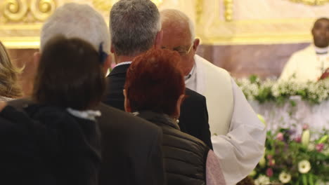 Gente-Haciendo-Cola-Y-Un-Anciano-Sacerdote-Dando-El-Pan-Sacramental-Durante-La-Celebración-De-La-Primera-Comunión