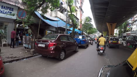 Rickshaw-driving-in-busy-urban-street-with-many-cars,-people,-overpass-visible