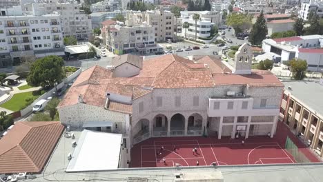 Überholschuss-Einer-Wunderschönen-Kirche-Vor-Einem-Basketballplatz,-Stadt-Larnaca,-Zypern