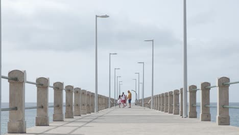 Summertime-scene-of-father-and-kids-walking-on-Porto-Santo-island-pier-by-ocean-sea-water-on-cloudy-day,-Portugal,-static