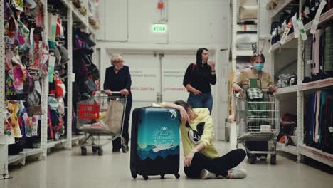 A-young-lady-is-sitting-on-the-floor-in-a-shopping-mall-with-a-suitcase