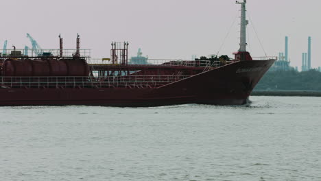 Vista-Cercana-Del-Petrolero-Navegando-Por-El-Puerto-En-Holanda,-Detrás-De-él-Trabajando-Molinos-De-Viento-Para-Producir-Energía.