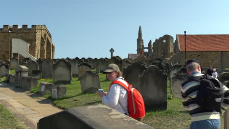 Tourists-walk-through-old-graveyard-in-Whitby,-North-Yorkshire,-UK-on-a-hot-summer-day