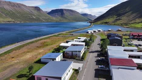 Aerial-View-of-Sudureyri-Fishing-Village-Buildings-and-Coastal-Road-in-Sunny-Landscape-of-Iceland