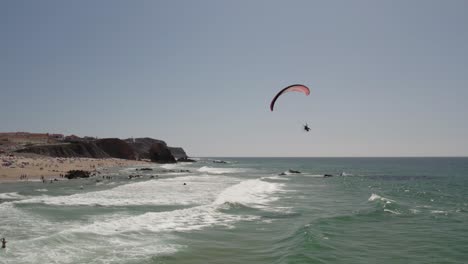 Aerial-view-of-Powered-Paraglide-flying-above-a-sunny-Santa-Cruz-Beach,-Portugal-Atlantic-Coast