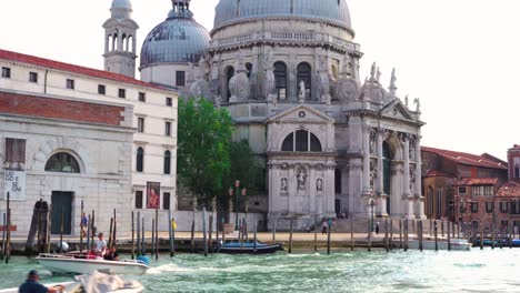 Venecia---Basílica-De-Santa-María-Della-Salute-Con-Un-Barco-A-Motor-Y-Góndolas-En-Los-Canales,-Vista-Desde-Un-Taxi-Acuático