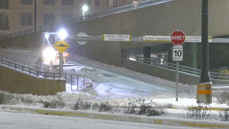 Niveladora-Bajando-Por-Una-Rampa-De-Estacionamiento-Elevada-Por-La-Noche-Empujando-Una-Carga-De-Nieve