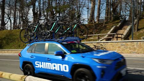 El-Coche-Azul-Del-Equipo-De-Carreras-Ciclistas-Pasa-Por-La-Carretera,-Filmado-En-Cámara-Lenta