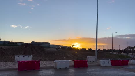 Vista-Estática-De-Una-Puesta-De-Sol-Desde-Un-Lugar-De-Trabajo-Con-Topadoras-Y-Contenedores.