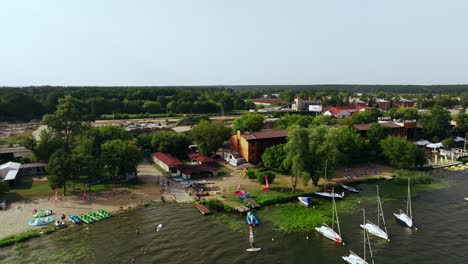 Aerial-View-of-Zagrze-Lake-Coast-on-Summer-Day,-Kite-Club,-People-and-Boats,-Drone-Shot