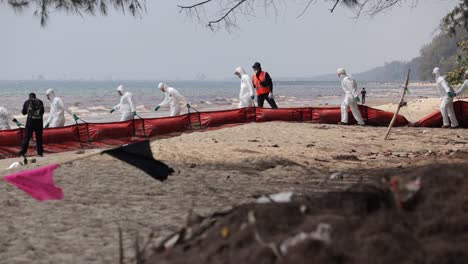 Derrame-De-Petróleo-En-La-Playa-De-Rayong,-Tailandia---Marina-Con-Traje-De-Ppe-Llevando-Un-Auge-Petrolero-En-La-Playa-Para-Controlar-La-Propagación-Del-Petróleo.