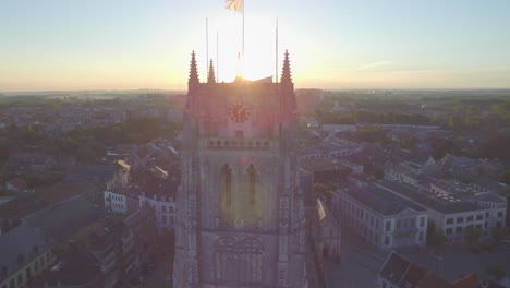 AERIAL:-Shot-of-a-church-tower-with-the-sun-coming-up-creating-sun-streaks